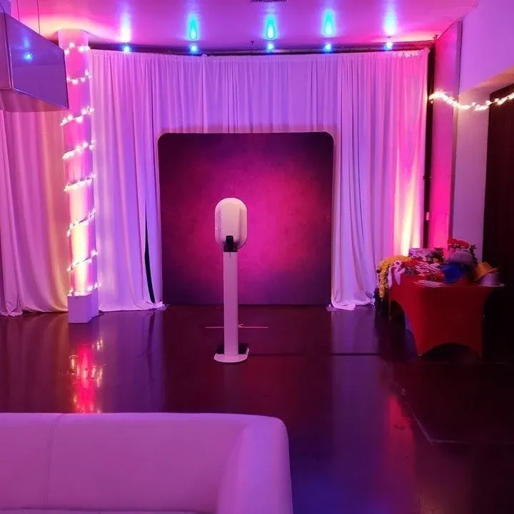 Photo booth against a pink draped wall under purple uplighting