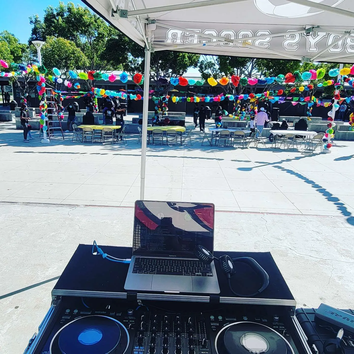 Outdoor DJ setup under a canopy strung with papel picado