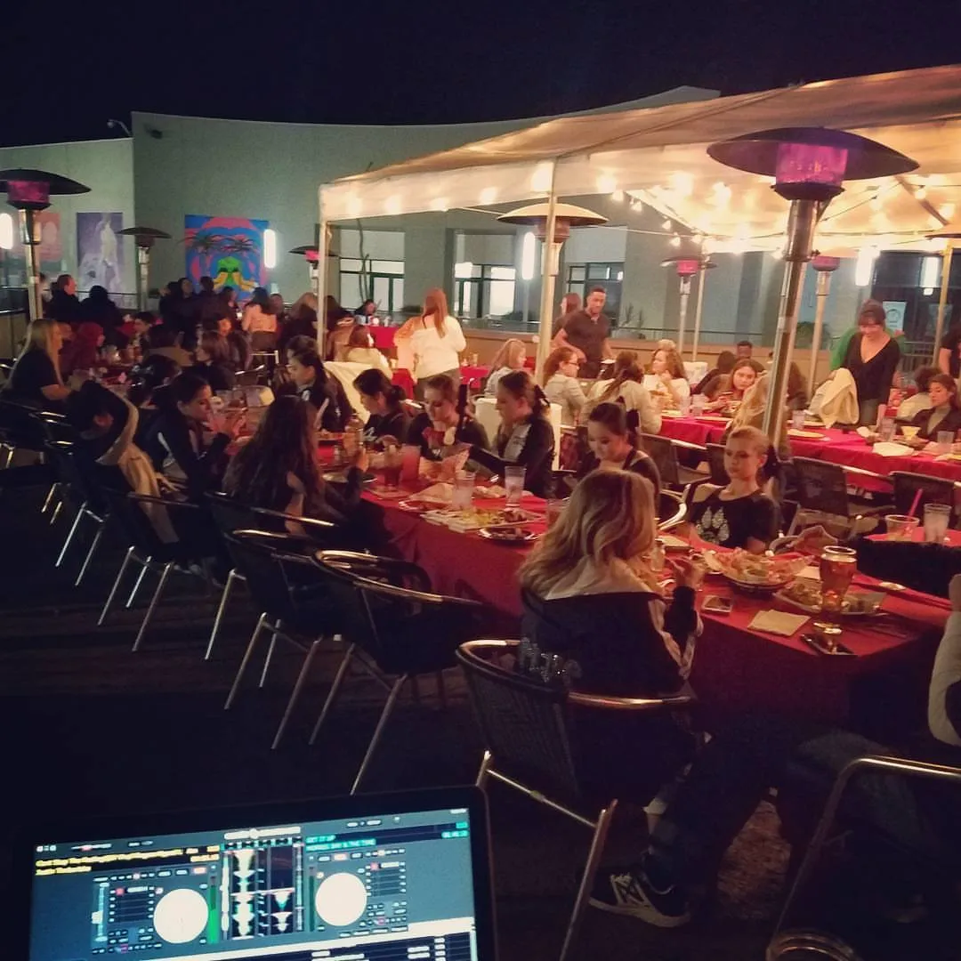 Large outdoor banquet under heaters, seen from the DJ position